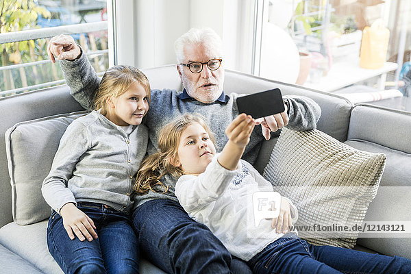 Zwei Mädchen und Großvater auf dem Sofa  die einen Selfie nehmen.
