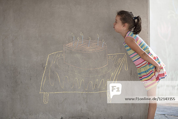 Girl pretending to blow out chalk birthday cake and candle drawing on concrete wall