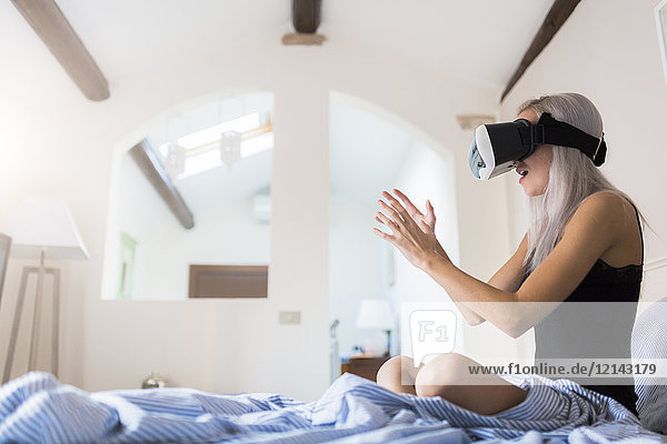 Amazed young woman sitting in bed wearing VR glasses