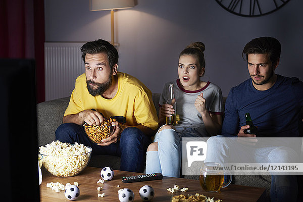 Aufgeregte Freunde die auf dem Sofa sitzen und fernsehen.