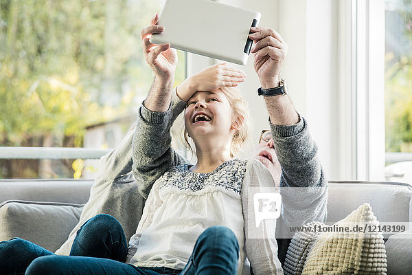 Zwei glückliche Mädchen und Großvater auf dem Sofa  die einen Selfie mit Tablette nehmen.