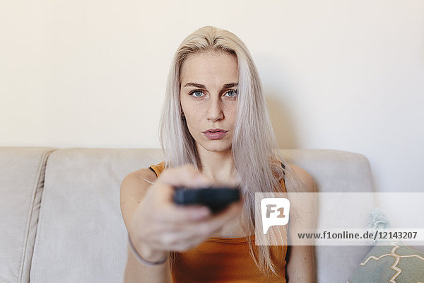 Young woman sitting on couch at home with remote control