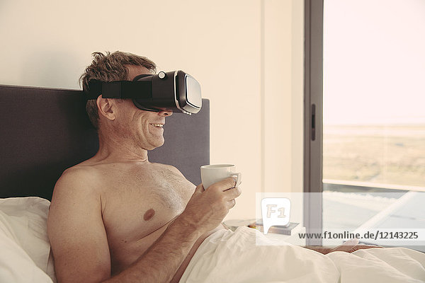 Mann mit VR-Brille im Bett mit Kaffeetasse
