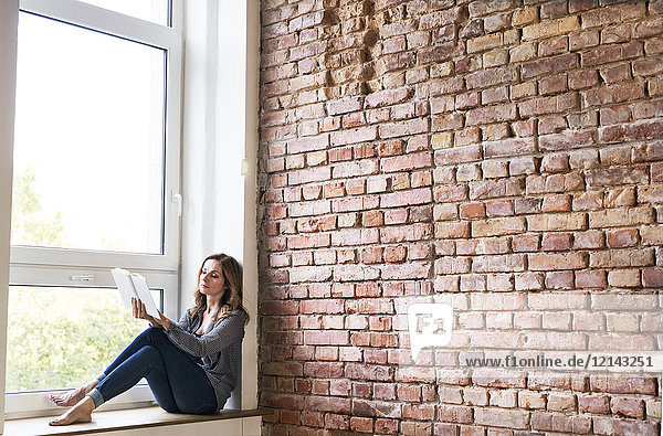 Woman sitting at home on the window sill  reading a book