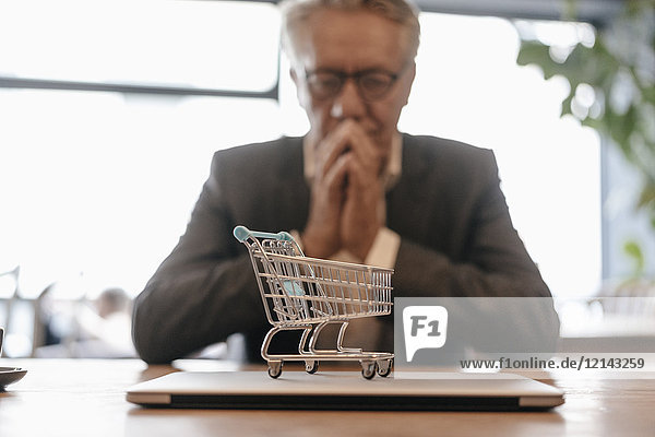 Senior businessman looking at shopping cart on laptop