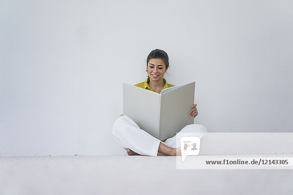 Lächelnde Frau sitzt auf dem Boden und liest ein überdimensionales Buch.