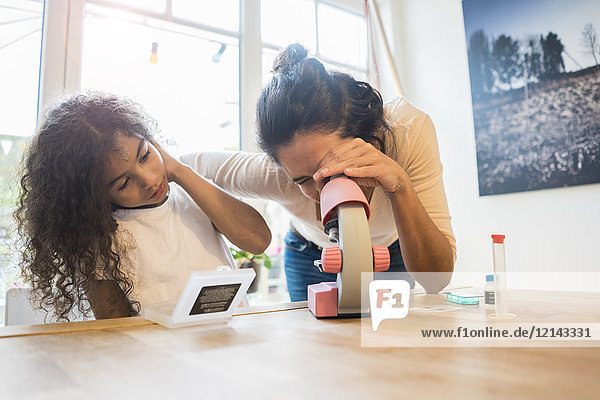 Mother helping daughter with homework  using microscope