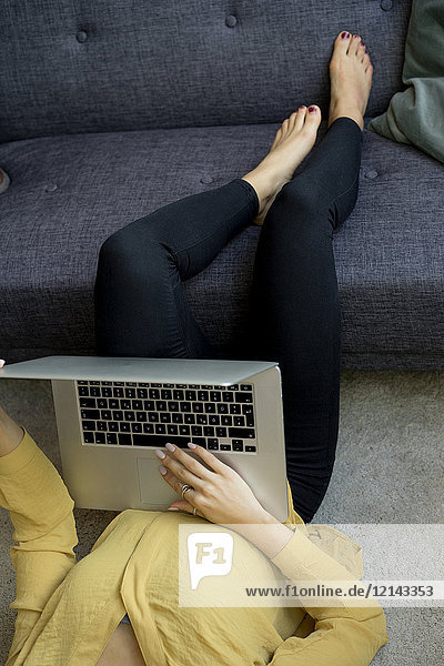 Junge Frau zu Hause im Wohnzimmer liegend mit Laptop