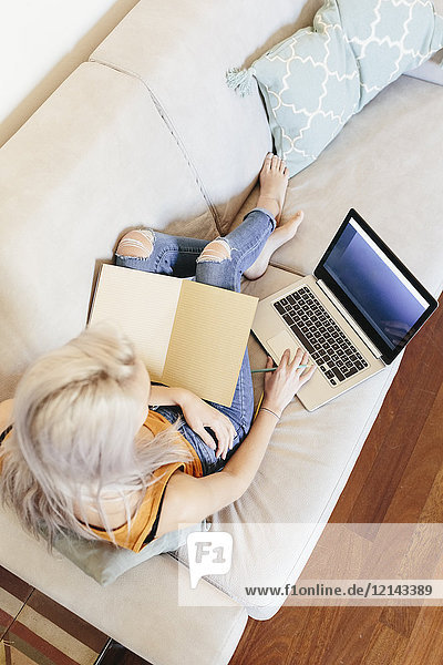 Junge Frau mit Notebook und Laptop auf der Couch zu Hause