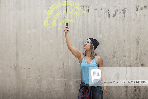 Frau hält Telefon auf der Suche nach einem Signal mit Wifi-Schild in gelber Kreide auf Betonwand