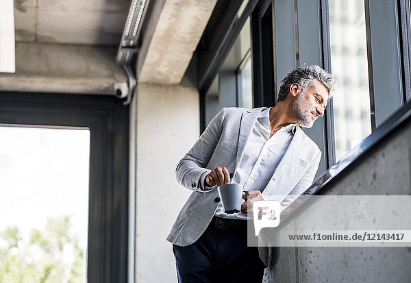 Smiling mature businessman with coffee mug looking out of window