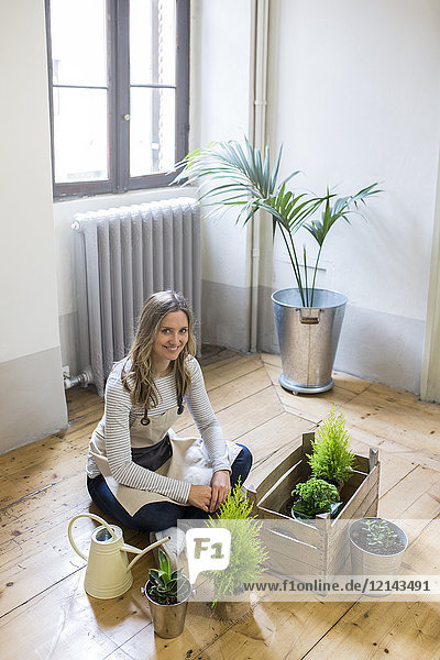 Porträt einer lächelnden Frau  die zu Hause auf dem Boden sitzt und Pflanzen pflegt.