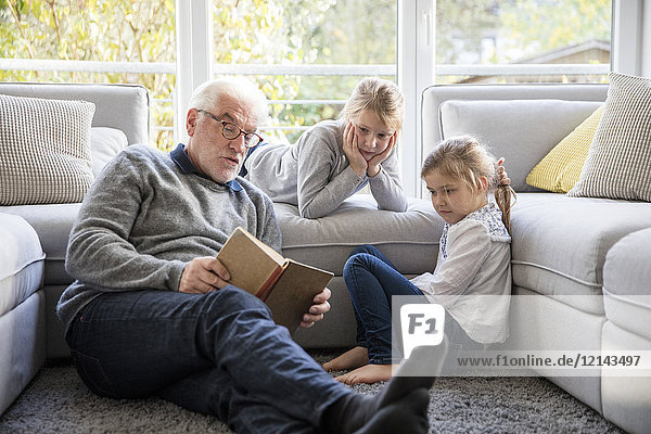 Zwei Mädchen und Großvater beim Lesen im Wohnzimmer