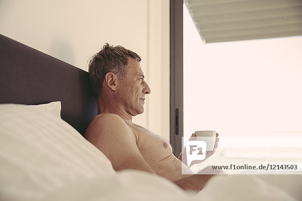 Entspannter Mann im Bett mit einer Tasse Kaffee