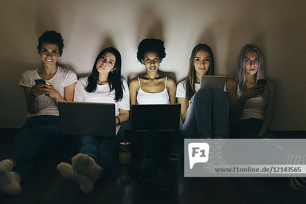 Group of female friends at home sitting on floor using technology in the dark