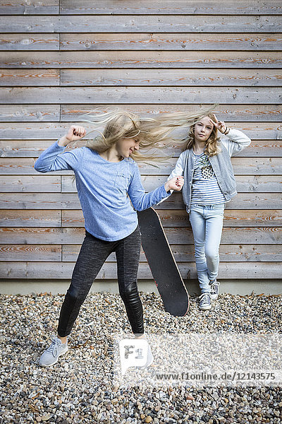 Zwei Mädchen mit Skateboard vor Holzfassade
