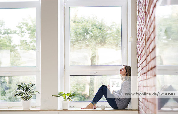 Woman sitting at home on the window sill  reading a book