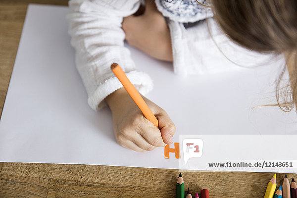 Girl writing letters on paper with colored pencil