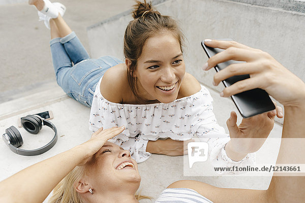 Zwei glückliche junge Frauen teilen sich ihr Handy in einem Skatepark.
