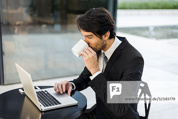 Businessman working on laptop and drinking coffee outdoors
