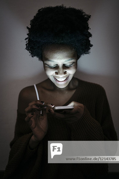 Lächelnde junge Frau mit Handy im Dunkeln