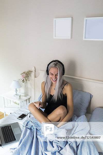 Happy young woman in bed with cell phone and headphones