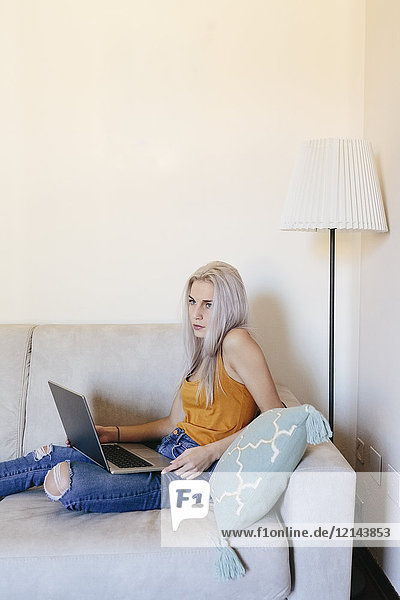 Junge Frau mit Laptop auf der Couch zu Hause
