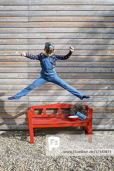 Mädchen springt in die Luft vor einer Holzfassade