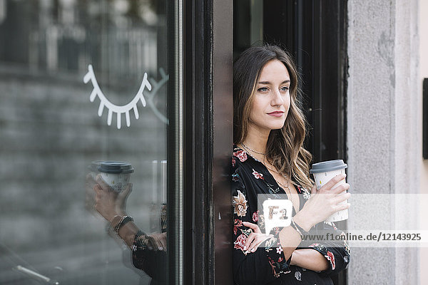 Porträt einer modischen Frau mit Kaffee zum Mitnehmen an der Eingangstür ihres Ladens