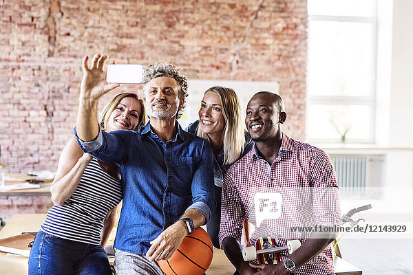 Glückliche Kollegen mit Basketball im Büro  die einen Selfie nehmen