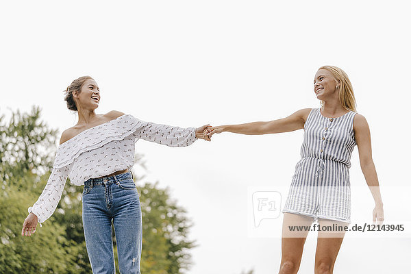 Zwei glückliche junge Frauen  die im Freien Händchen halten.