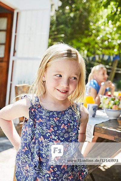 Porträt des lächelnden Mädchens mit Mutter im Hintergrund am Gartentisch