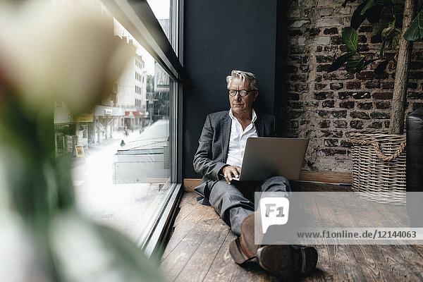 Businessman sitting on floor next to window  using laptop