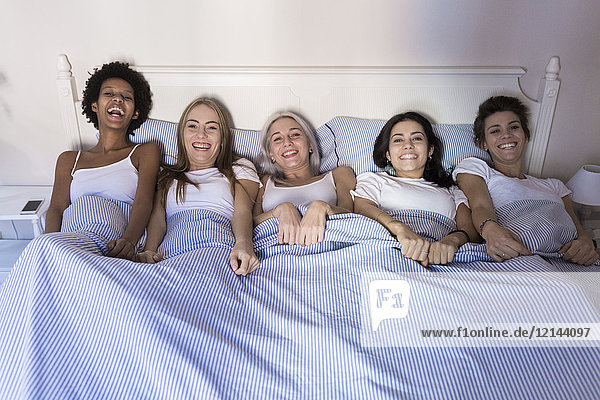 Portrait of happy female friends lying in bed side by side