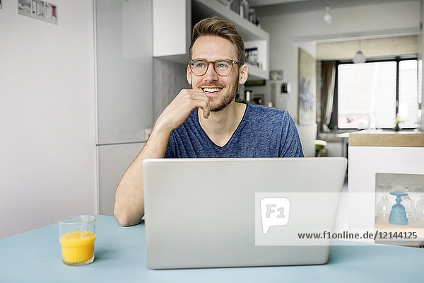 Porträt eines lächelnden Mannes mit Laptop in der Küche zu Hause