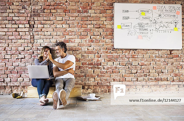 Geschäftsmann und Frau sitzen in einem Loft  geben High Five  gründen ein Start-up-Unternehmen