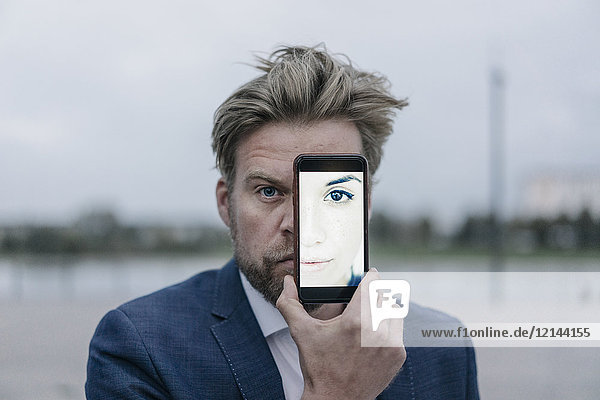 Businessman holding cell phone with image of a woman in front of his eyes