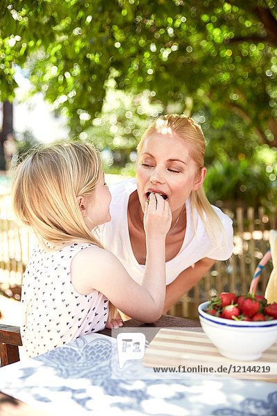 Girl feeding mother with stawberries
