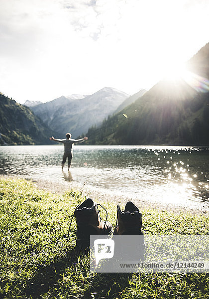Austria  Tyrol  hiking shoes and man standing with outstretched arms in mountain lake