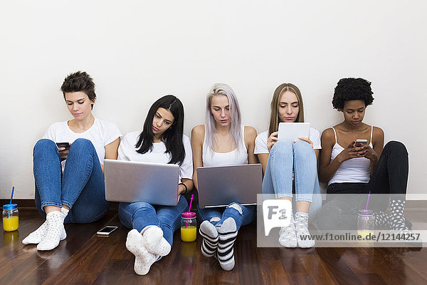 Gruppe von Freundinnen zu Hause auf dem Boden sitzend mit Technik
