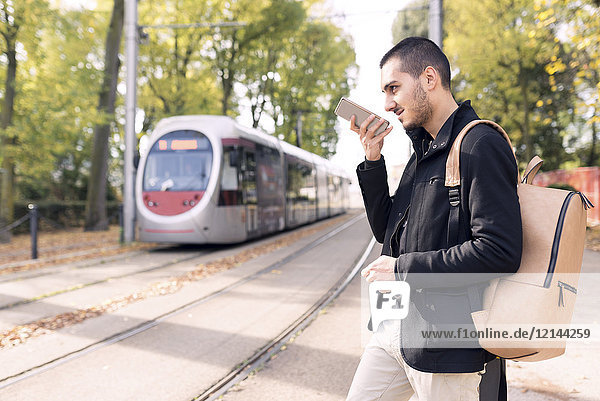 Junger Mann mit Handy an der Straßenbahnhaltestelle im Freien
