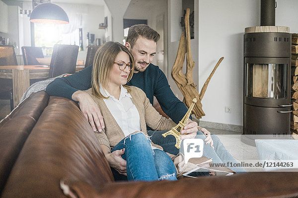 Lächelndes Paar auf der Couch zu Hause mit Tablett und Eiffelturm-Modell