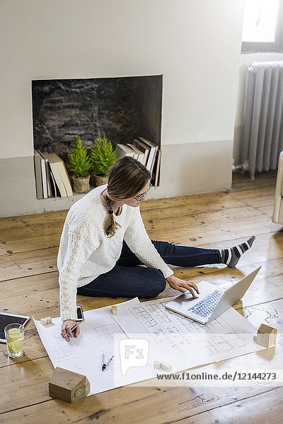 Woman sitting on the floor with blueprint and laptop
