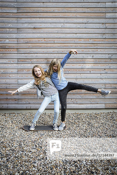 Zwei lachende Mädchen amüsieren sich vor einer Holzfassade