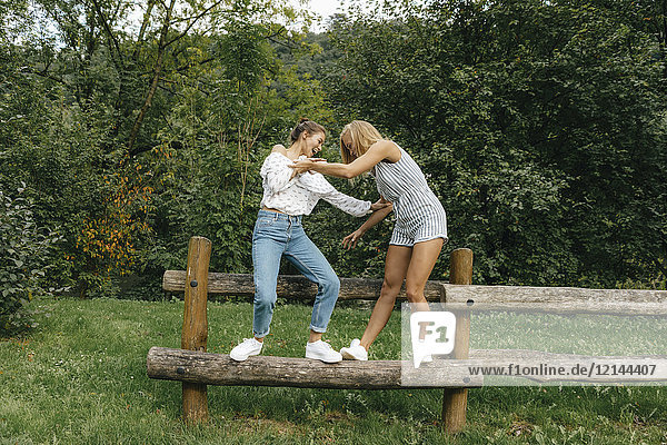 Zwei glückliche junge Frauen  die auf einem Zaun in einem Park balancieren.