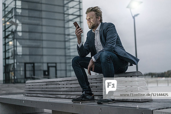 Businessman sitting on bench in the city holding cell phone
