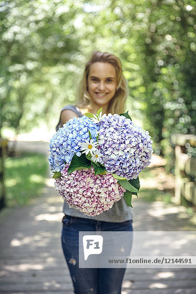 Smiling young woman showing a bouquet of hydrangeas and daisies