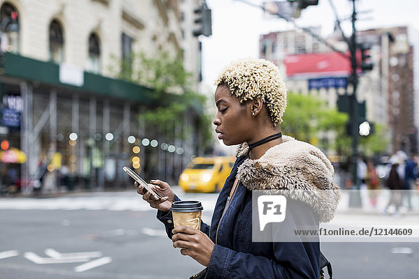 USA  New York City  fashionable young woman with coffee to go looking at cell phone on the street
