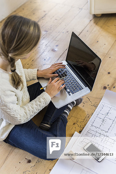 Woman sitting on the floor with blueprint using laptop