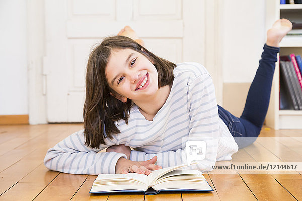 Porträt eines glücklichen Mädchens auf dem Boden liegend mit Buch